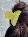 Yellow butterfly hair clip in a person's hair against a light gray brick wall.