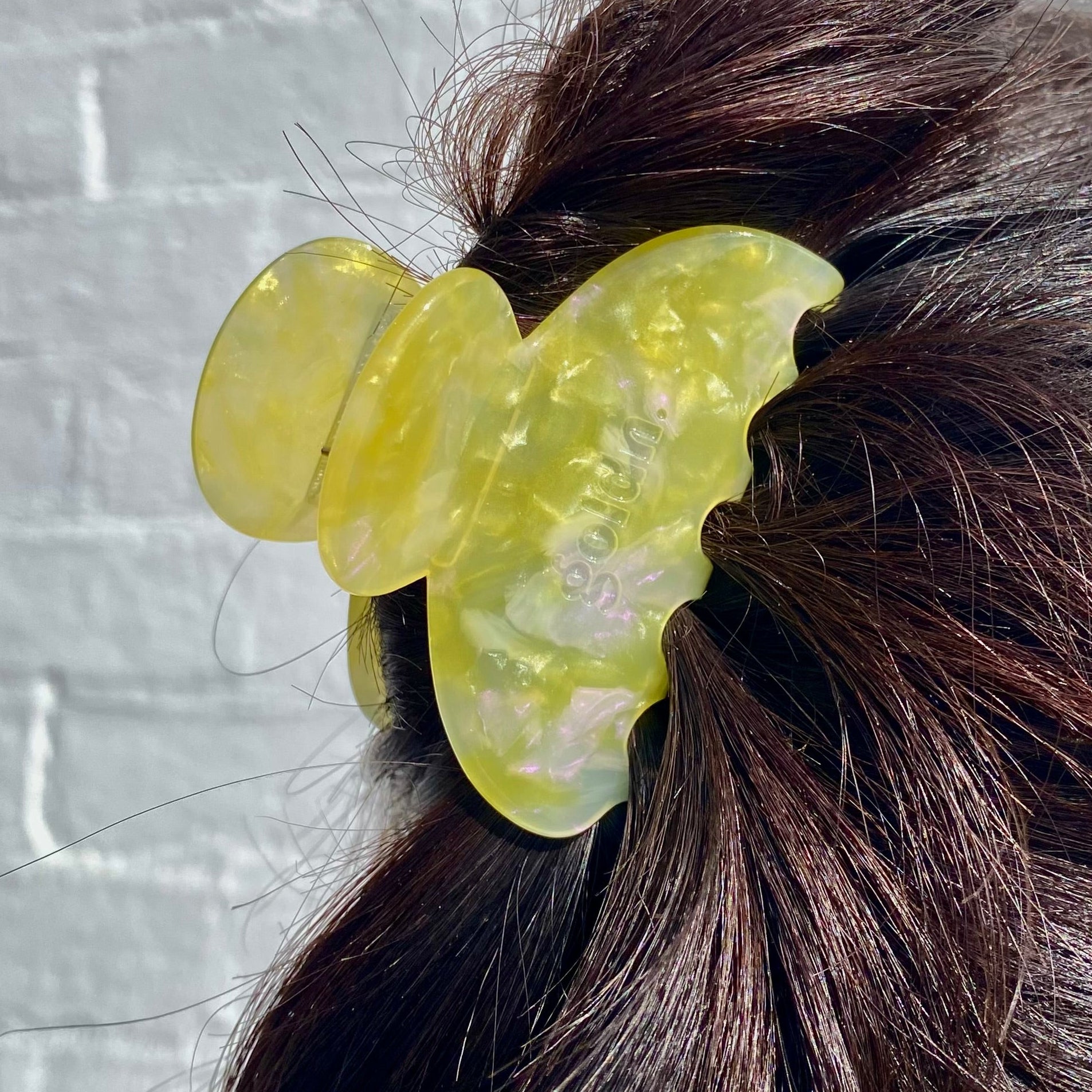 Yellow butterfly hair clip in a person's hair against a light gray brick wall.