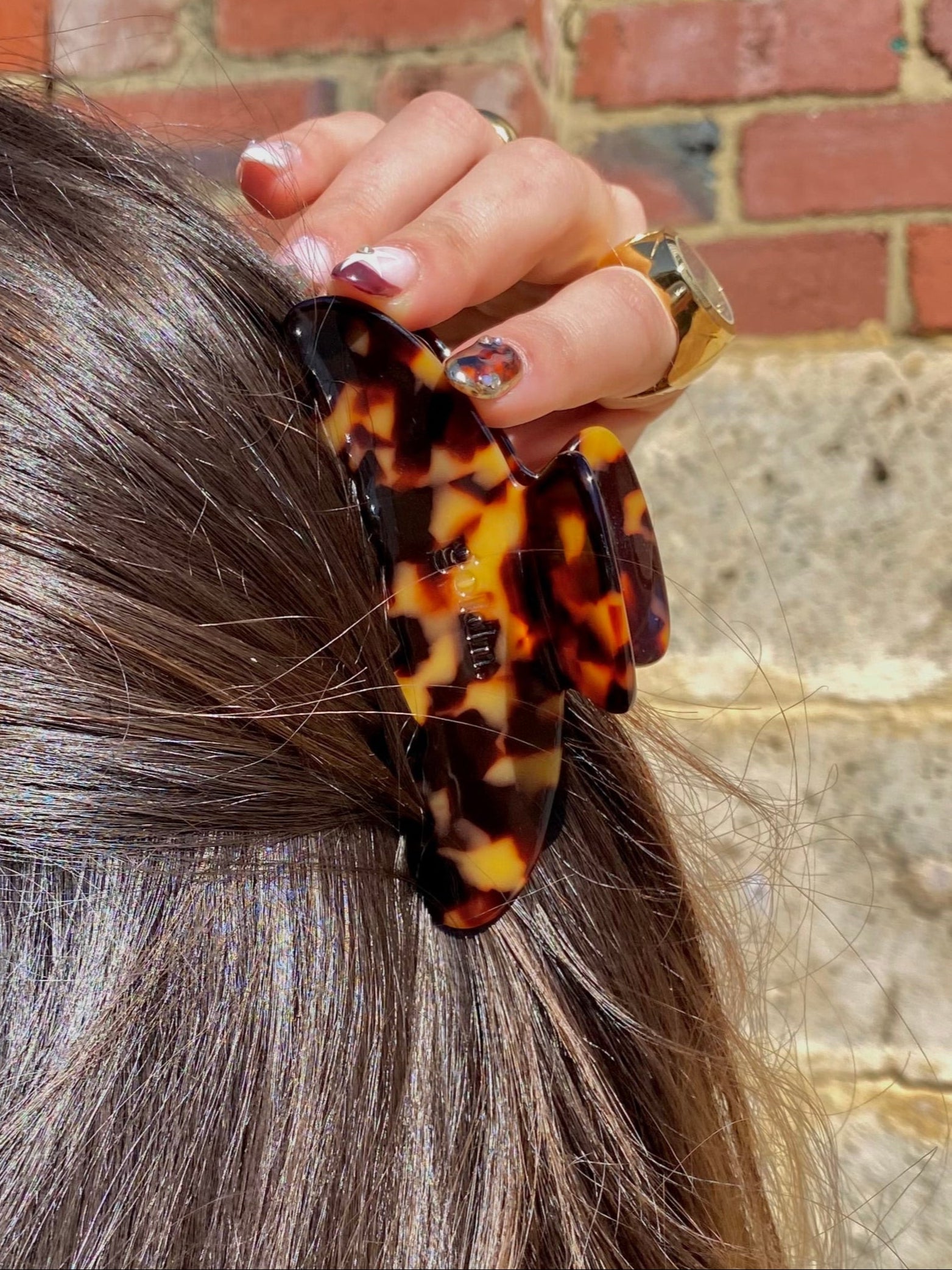 Person styling hair with a leopard print scrunchie against a brick wall.