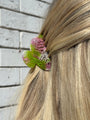 Close-up of a hair tie with pink and green design in a person's hair on a wooden floor background.