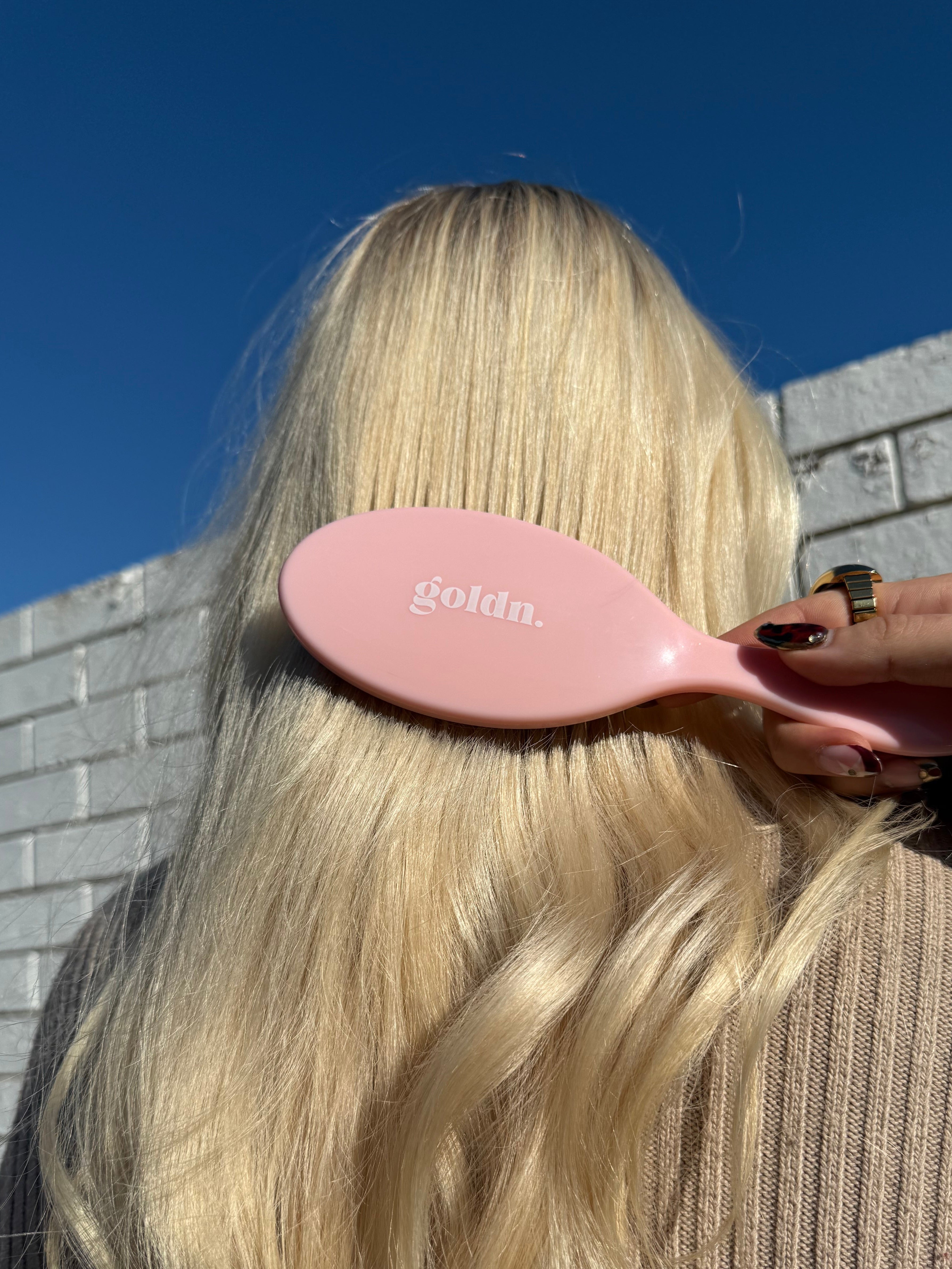 Person using a pink hairbrush on their blonde hair with a blue background