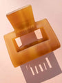 Translucent amber Lounge Claw Clip Small with rectangular cutout, casting shadow on pink surface for aesthetic appeal.