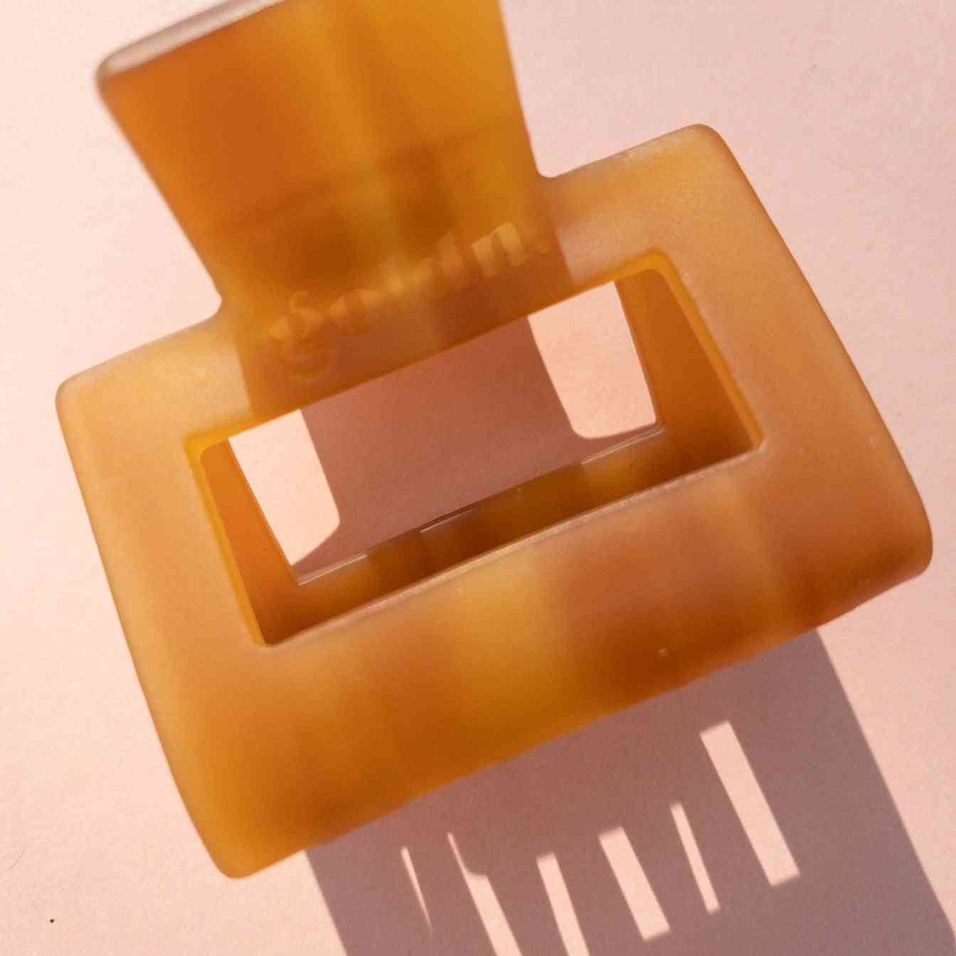 Translucent amber Lounge Claw Clip Small with rectangular cutout, casting shadow on pink surface for aesthetic appeal.