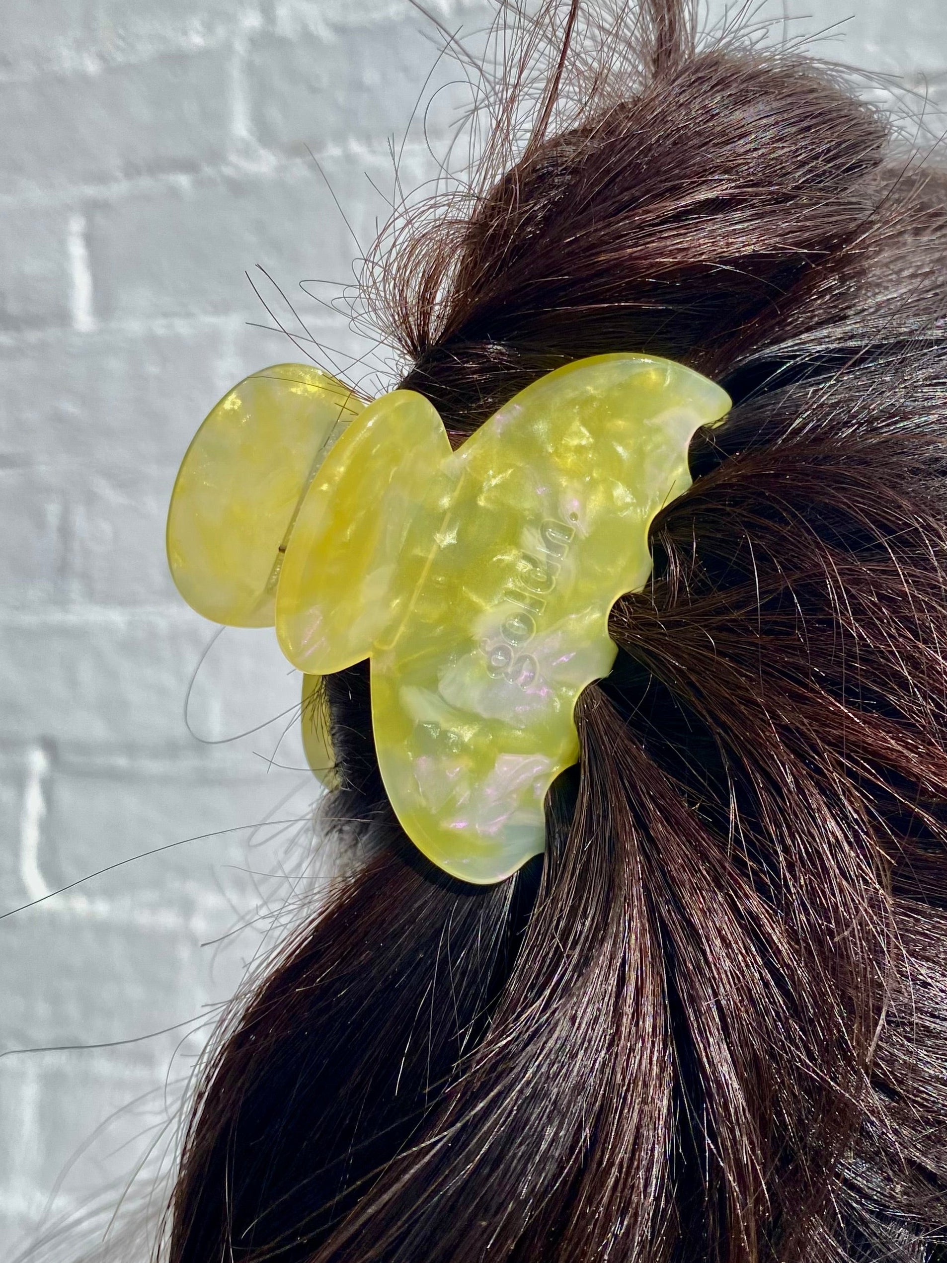Yellow butterfly hair clip in a person's hair against a light gray brick wall.
