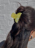 Person with a yellow butterfly hair clip in their dark hair against a gray brick wall.