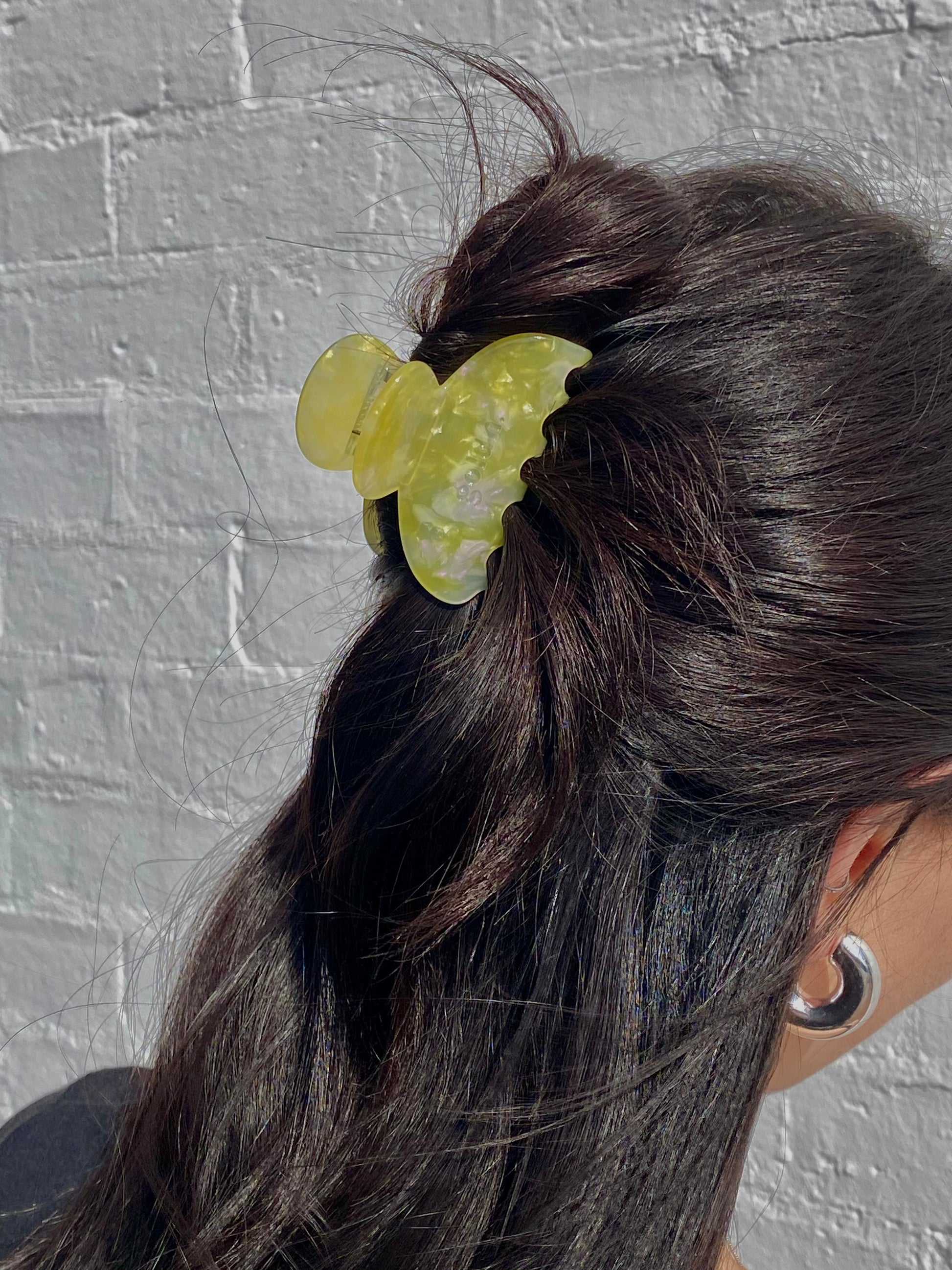 Person with a yellow butterfly hair clip in their dark hair against a gray brick wall.