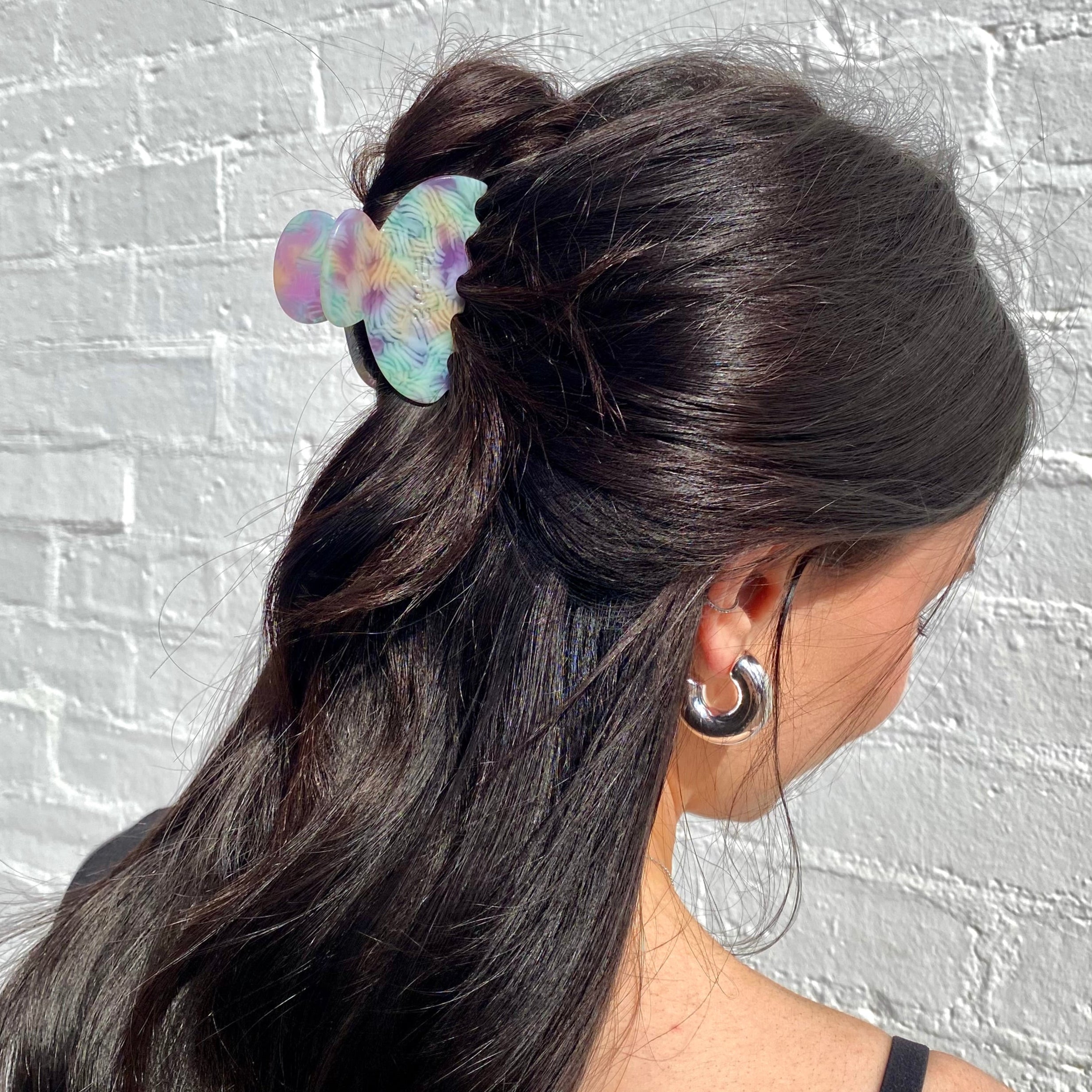 Woman with a ponytail featuring a colorful hair tie against a gray brick wall.