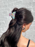 Woman with a ponytail featuring a colorful hair tie against a gray brick wall.