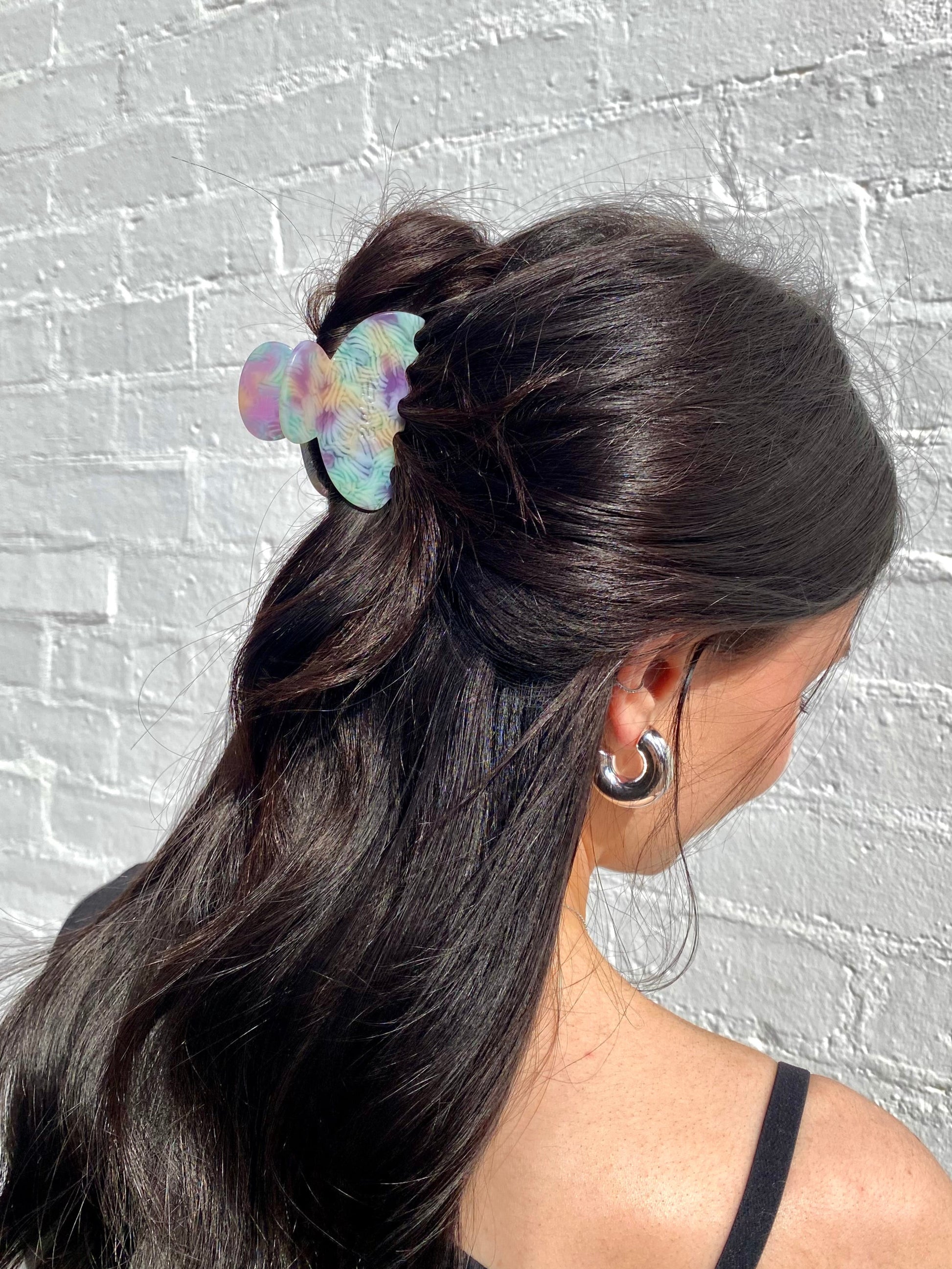 Woman with a ponytail featuring a colorful hair tie against a gray brick wall.