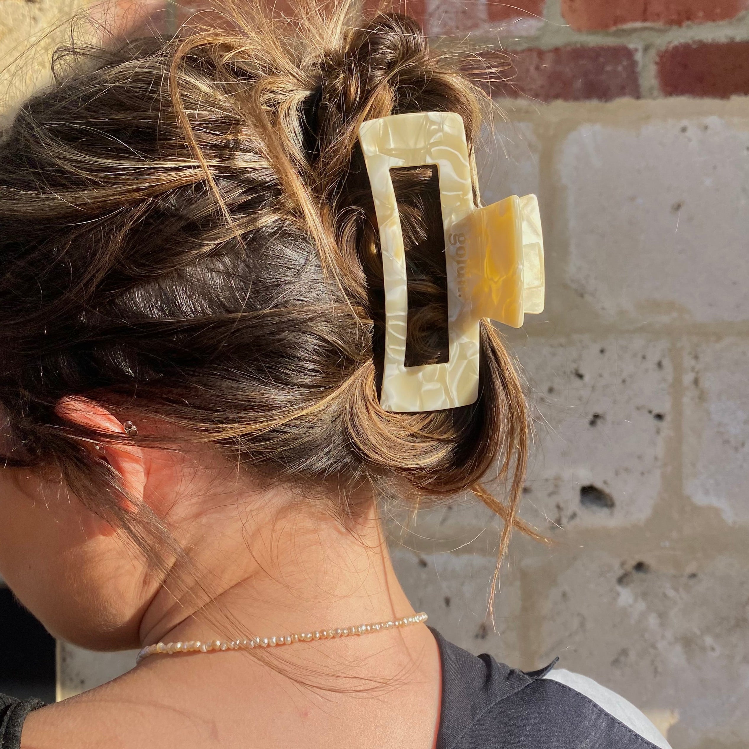 Person with a large hair clip in their hair against a brick wall.