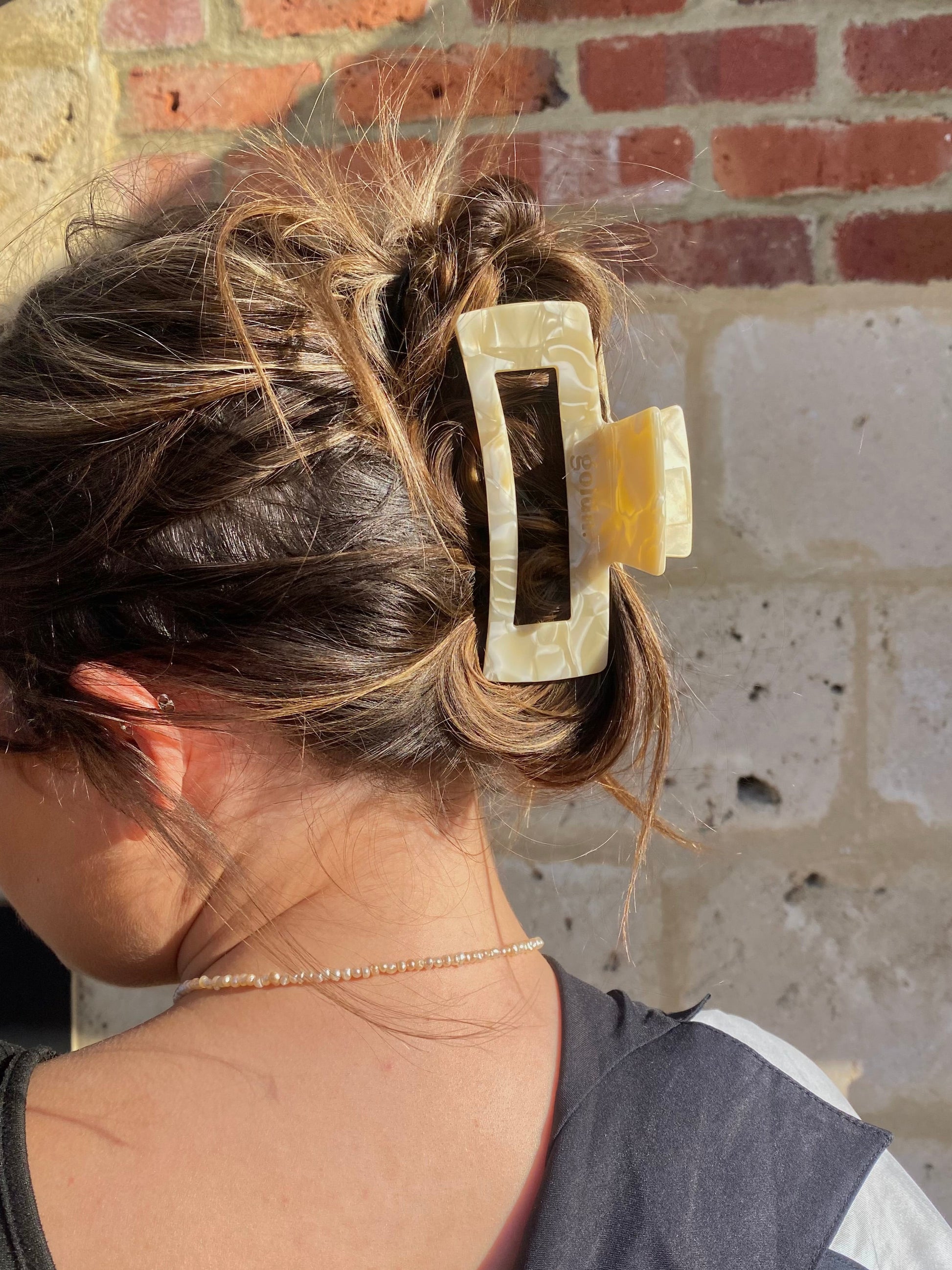 Person with a large hair clip in their hair against a brick wall.