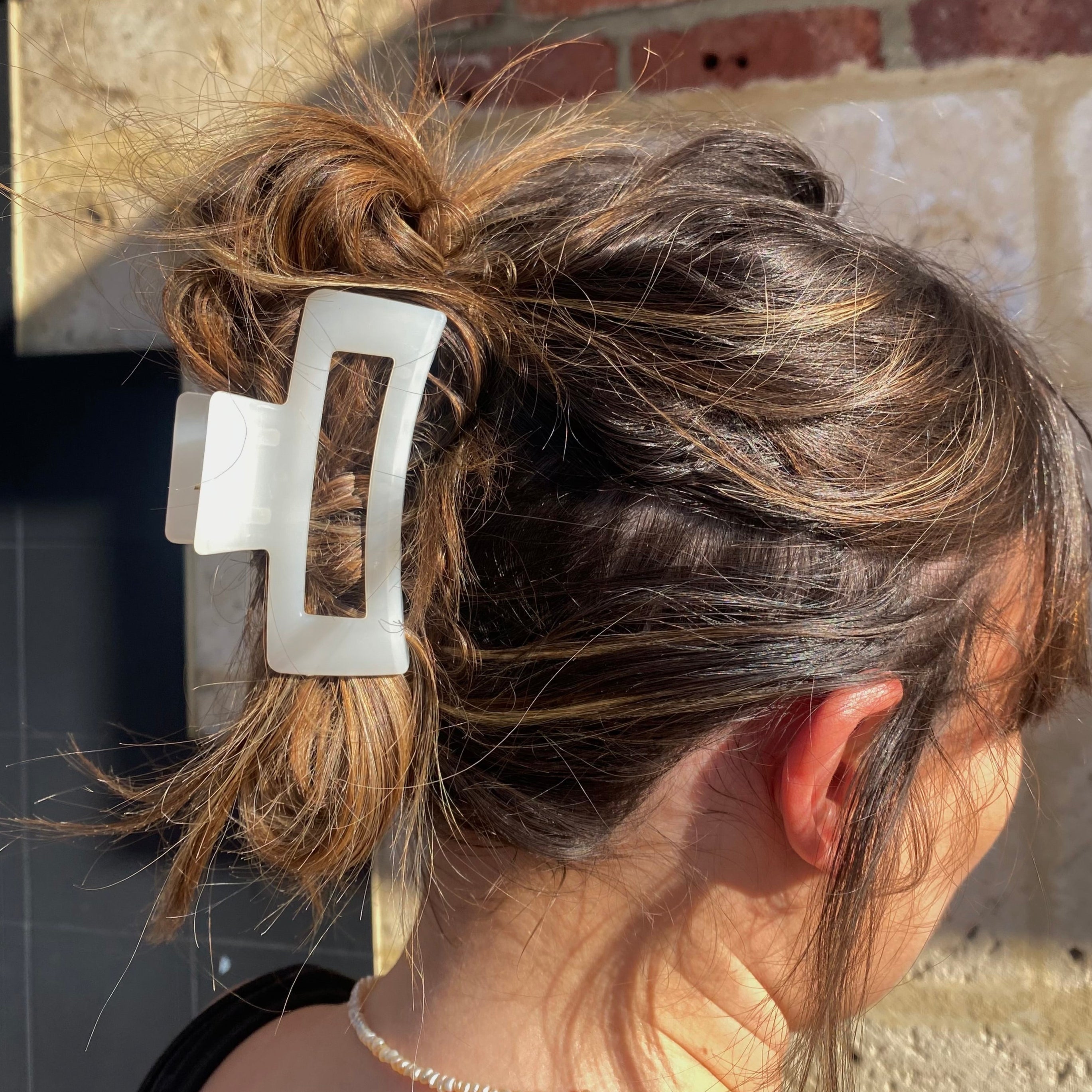 Person with a hair clip in their bun against a brick wall.
