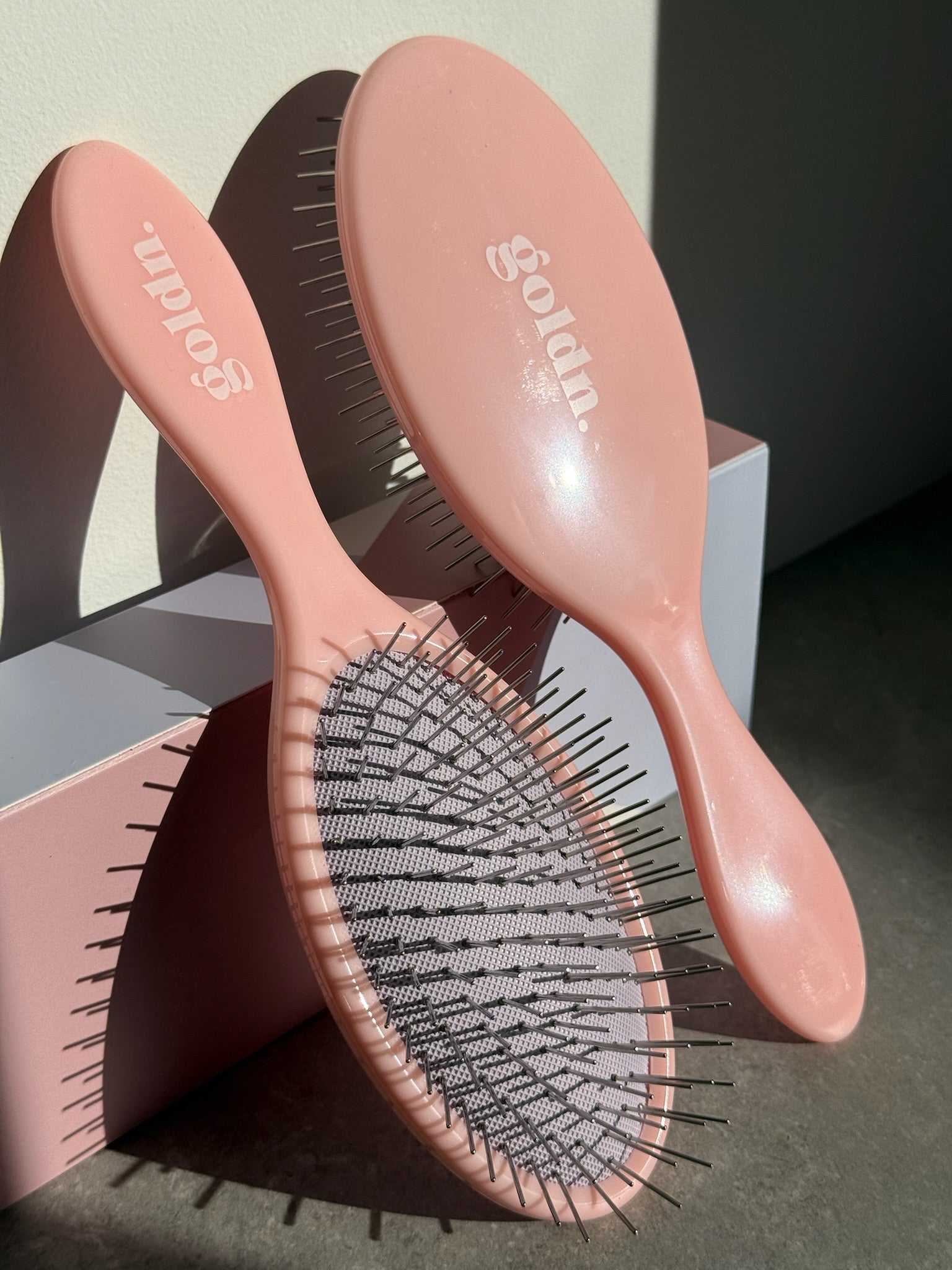 Pink hairbrushes with 'Gold'n' logo on a neutral background golden hour