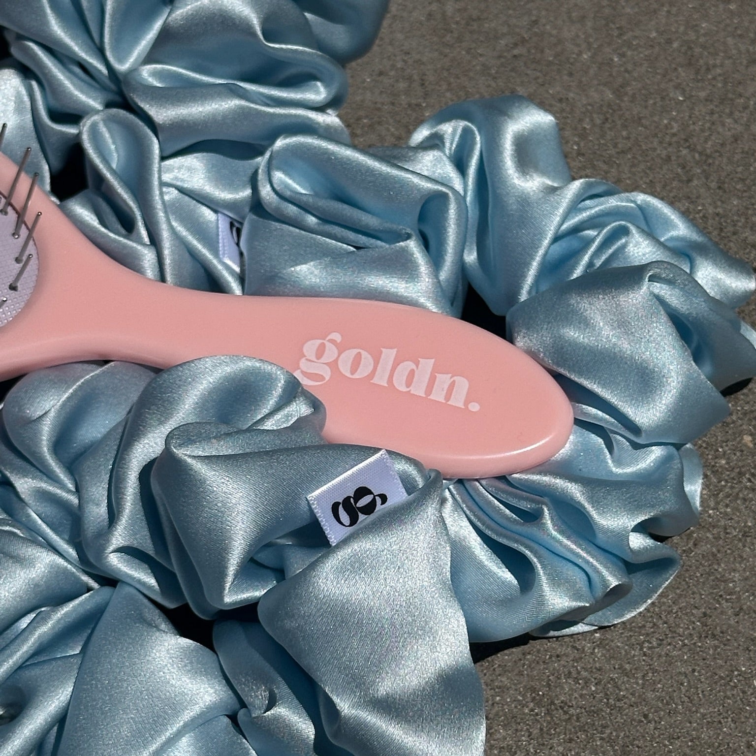 Pink hairbrush with 'gold'n' branding on blue satin scrunchies.