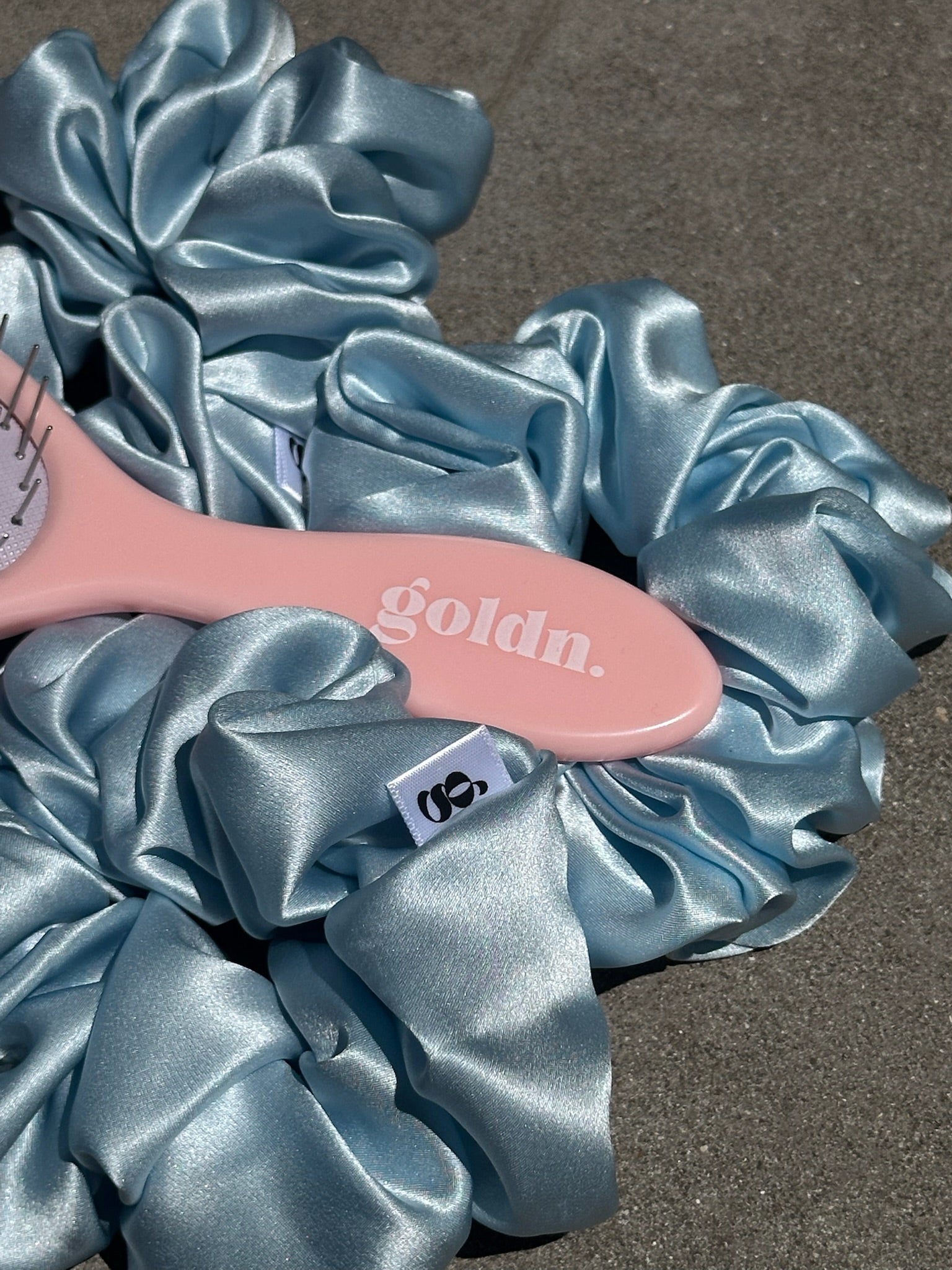 Pink hairbrush with 'gold'n' branding on blue satin scrunchies.