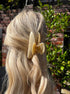 Close-up of a person with blonde hair wearing a beige hair clip outdoors.