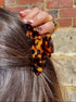 Person styling hair with a leopard print scrunchie against a brick wall.