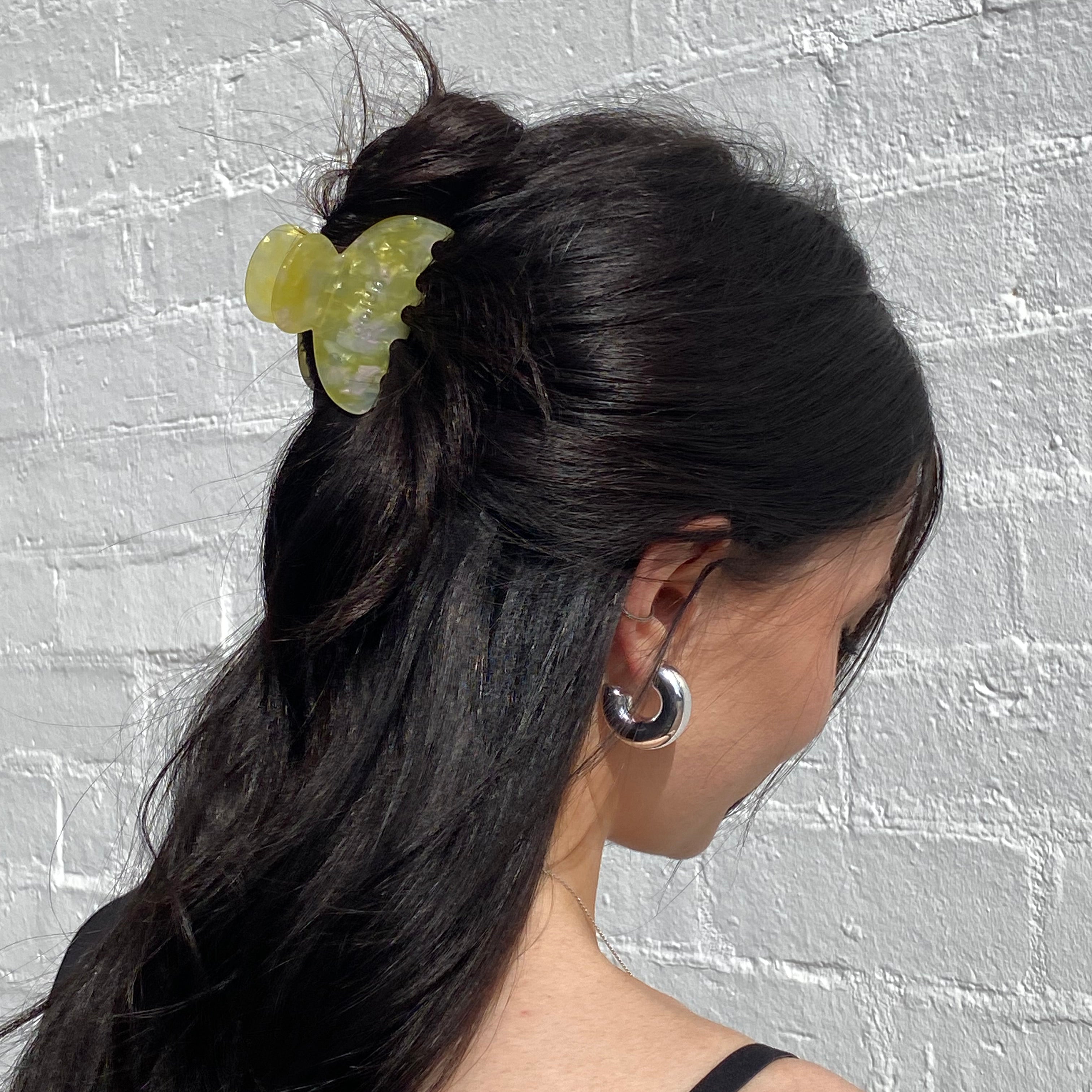 Person with long dark hair wearing a green hair tie against a textured gray background