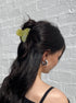 Person with long dark hair wearing a green hair tie against a textured gray background