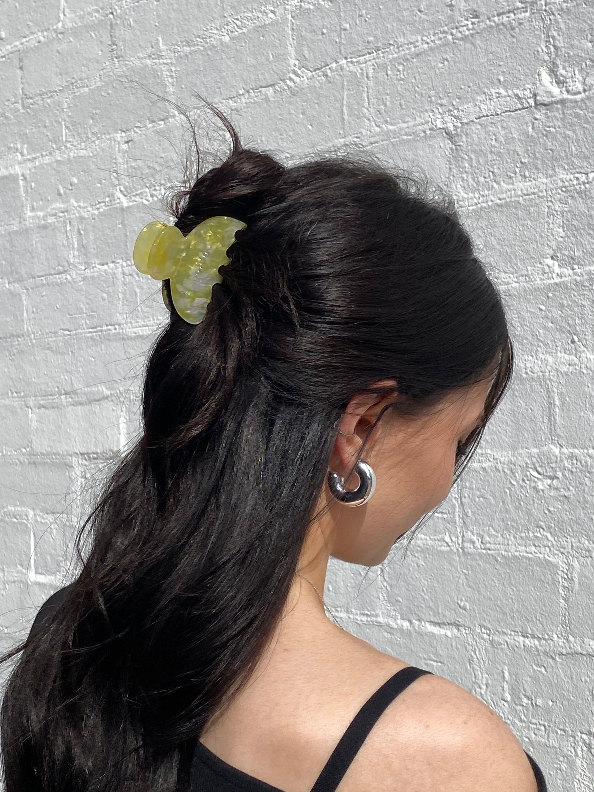 Person with long dark hair wearing a green hair tie against a textured gray background