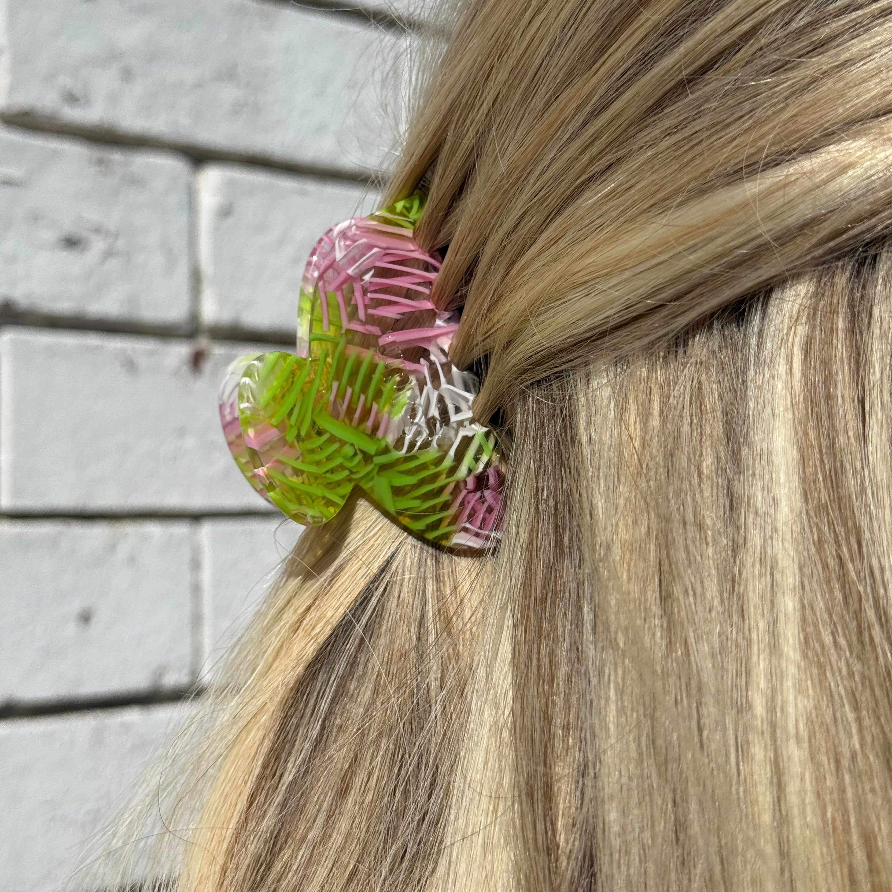 Close-up of a hair tie with pink and green design in a person's hair on a wooden floor background.