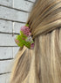 Close-up of a hair tie with pink and green design in a person's hair on a wooden floor background.