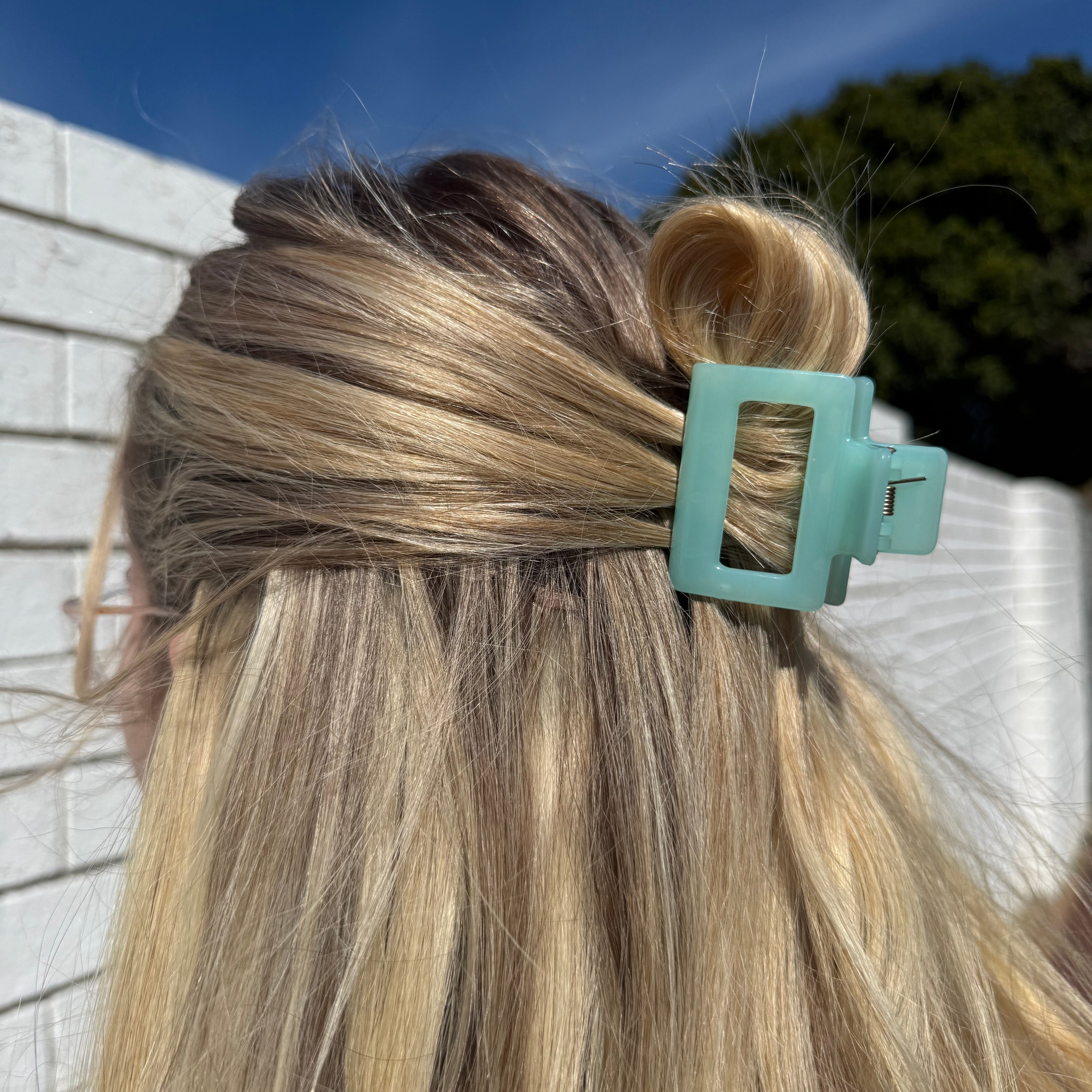 Close-up of a teal hair clip in blonde hair with a blurred outdoor background