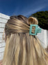Close-up of a teal hair clip in blonde hair with a blurred outdoor background