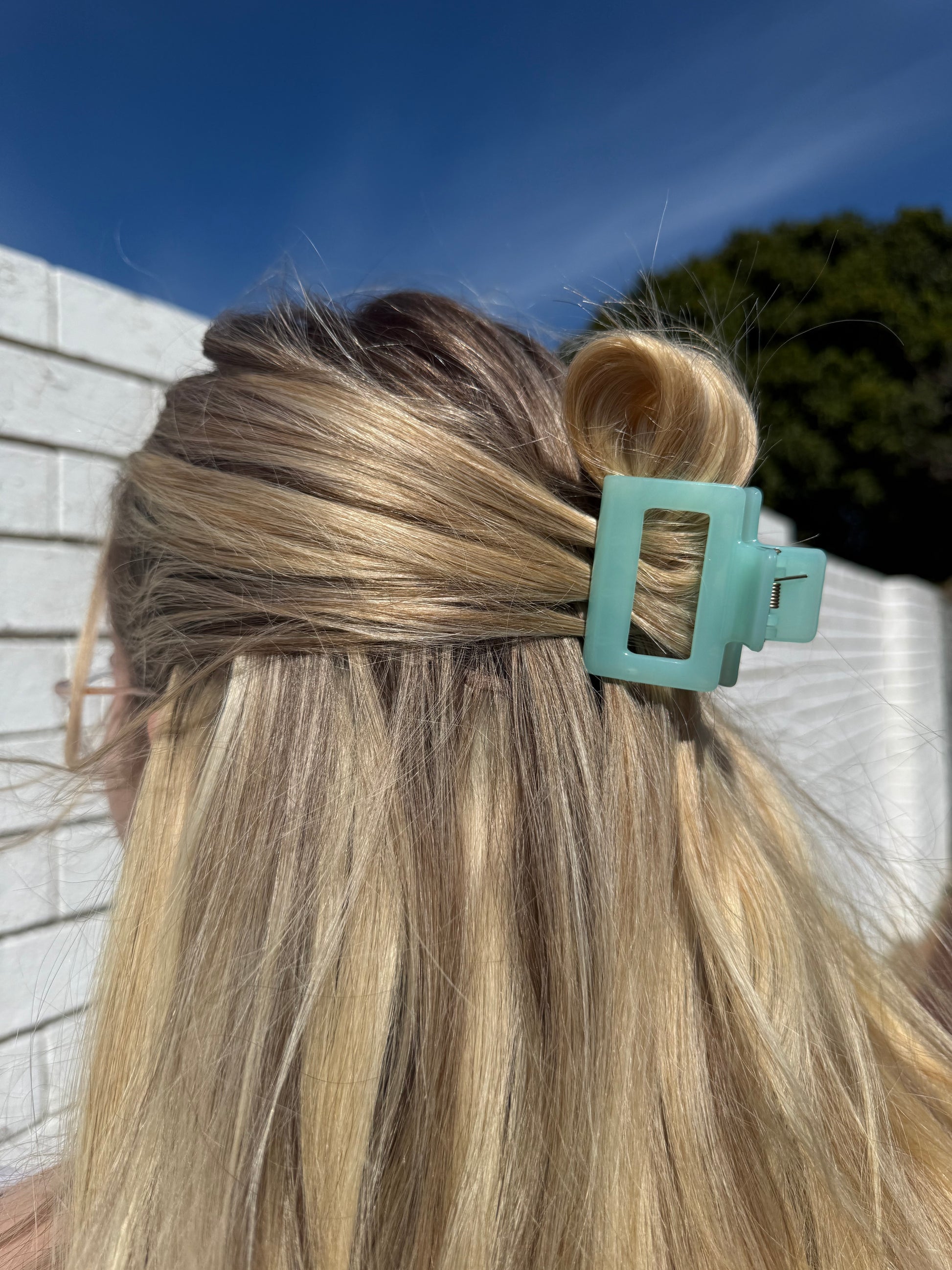 Close-up of a teal hair clip in blonde hair with a blurred outdoor background