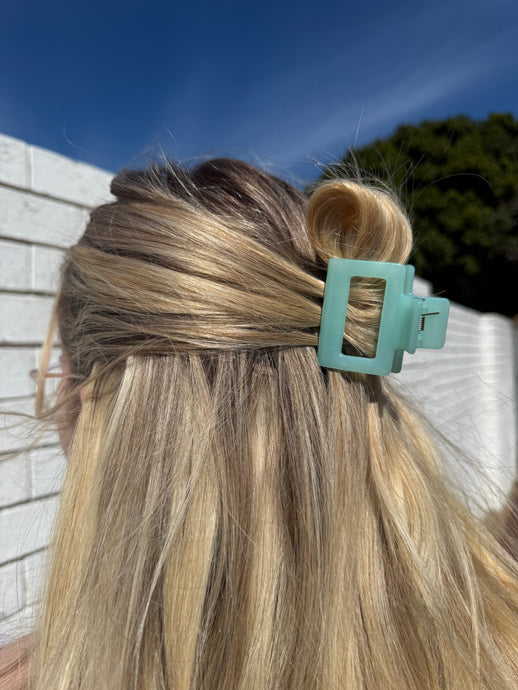 Close-up of a teal hair clip in blonde hair with a blurred outdoor background