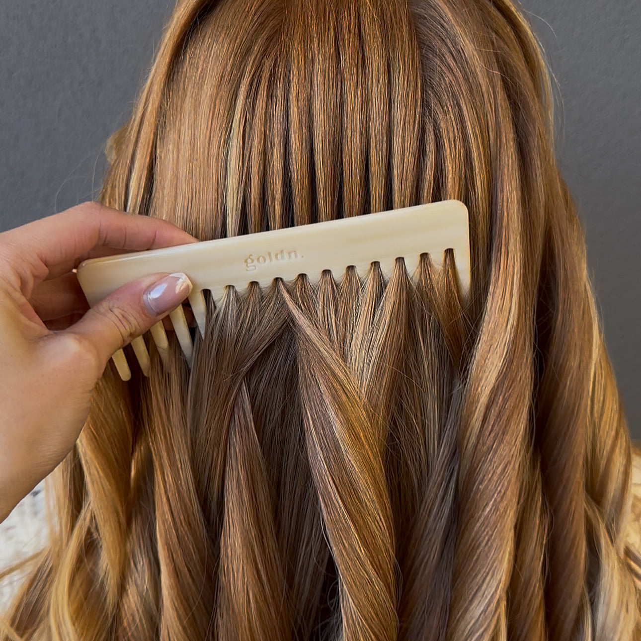 Person combing their long, wavy hair with a comb against a gray background