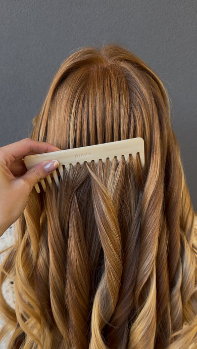 Person combing their long, wavy hair with a comb against a gray background
