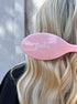 Pink hairbrush with 'goldn.' branding held by a person with blonde hair.