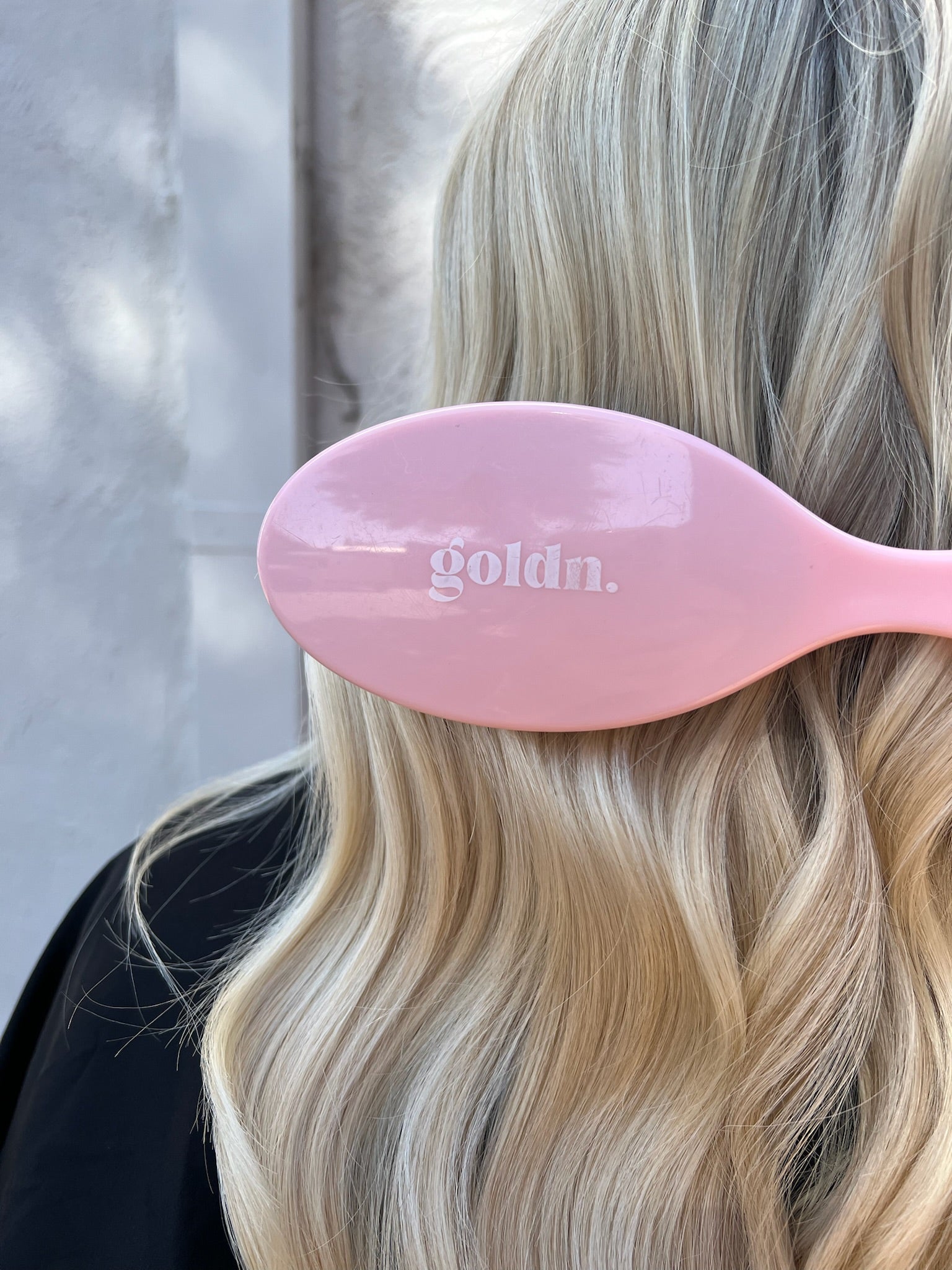 Pink hairbrush with 'goldn.' branding held by a person with blonde hair.