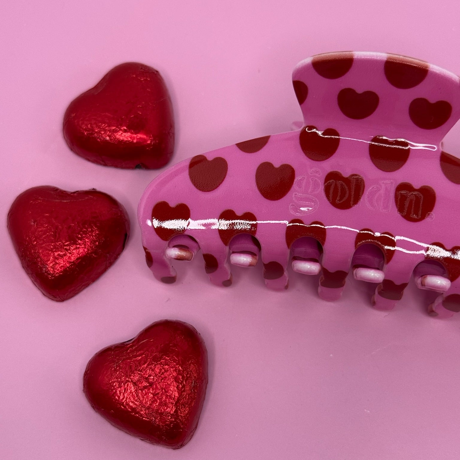 Pink hair clip with red heart patterns on a pink surface. Goldnwares Curve Clip with a heart pattern plate-based acetate hair clip for medium to thick hair.
