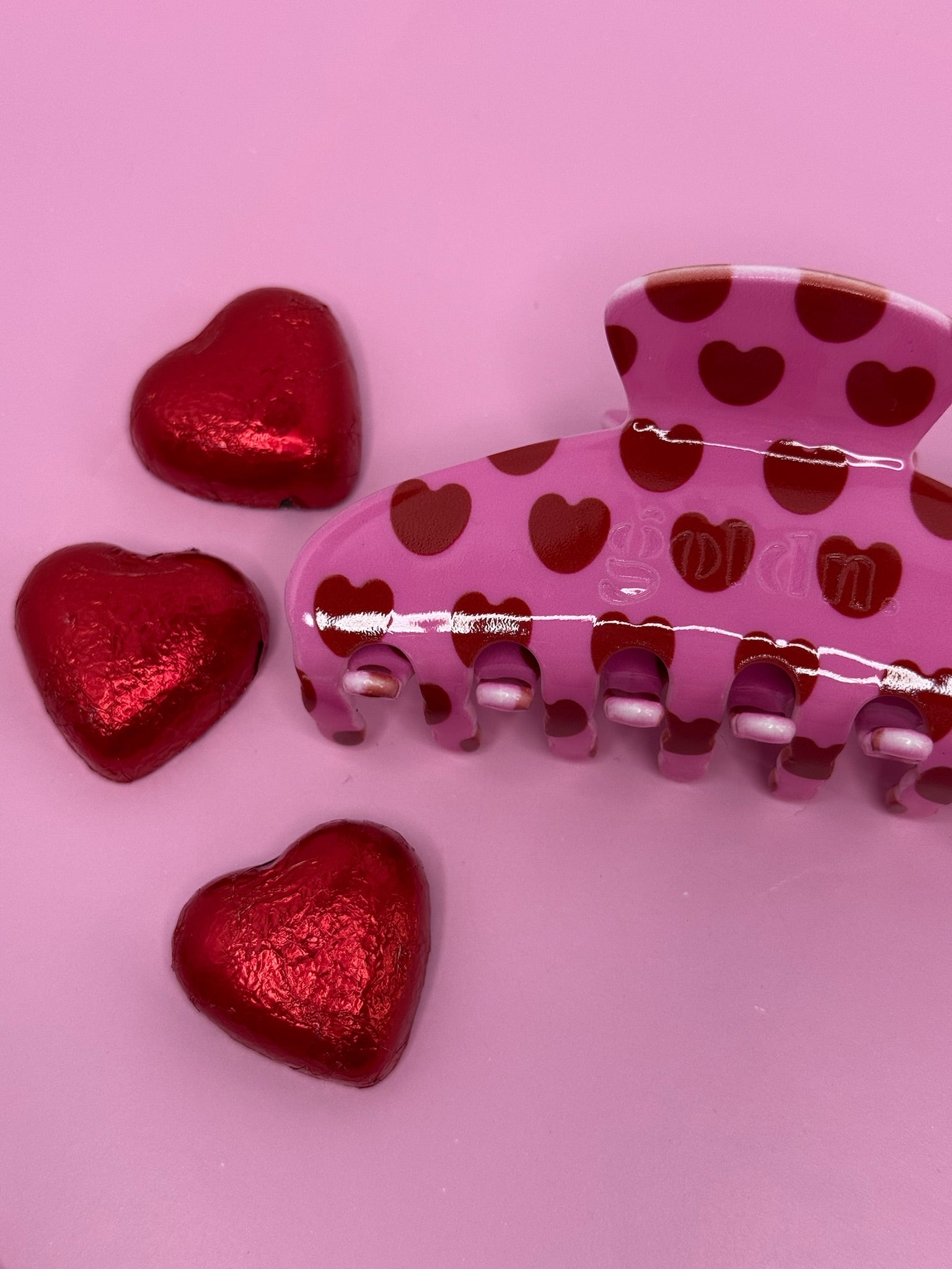 Pink hair clip with red heart patterns on a pink surface. Goldnwares Curve Clip with a heart pattern plate-based acetate hair clip for medium to thick hair.