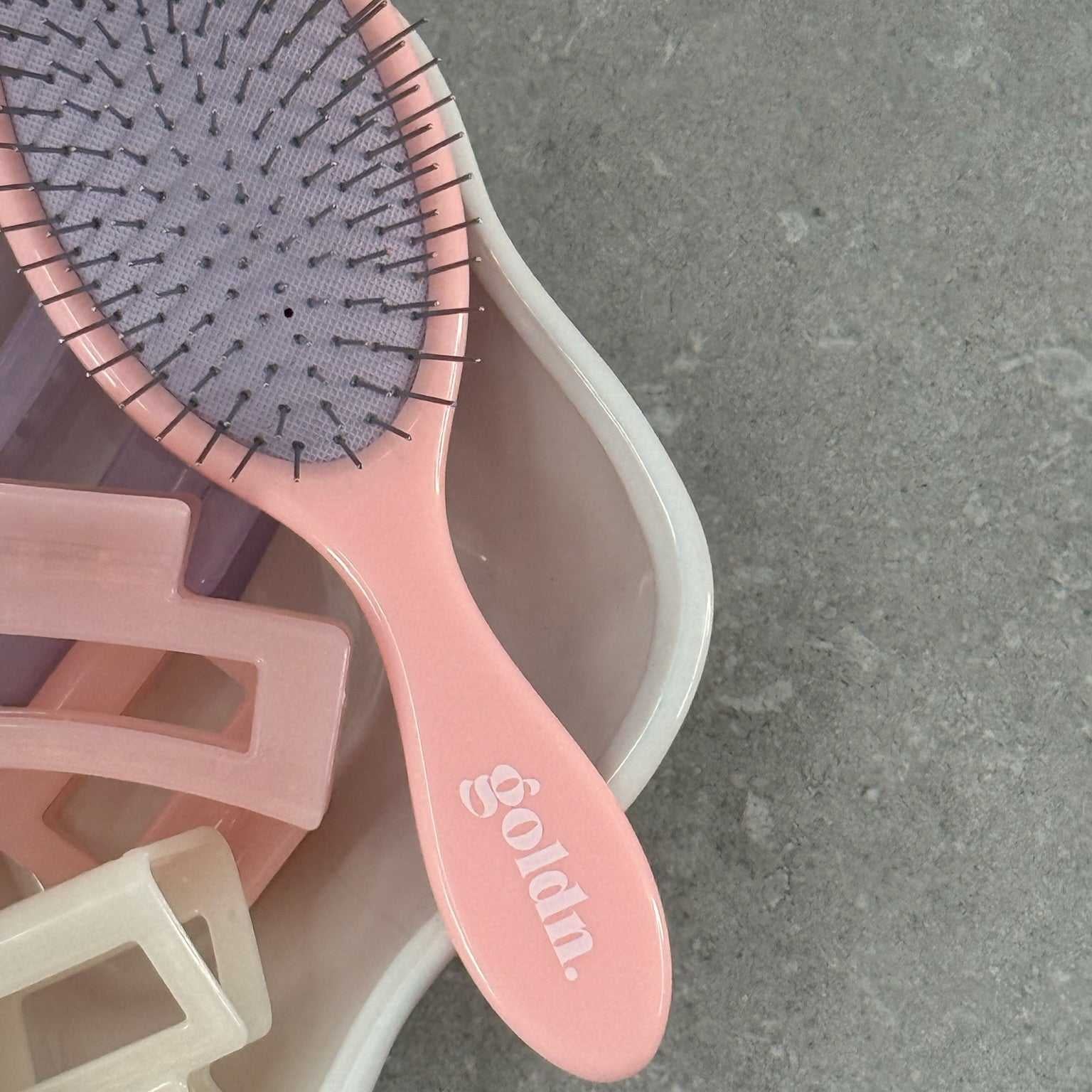 Pink hairbrush with bristle head and wooden clips on a gray surface