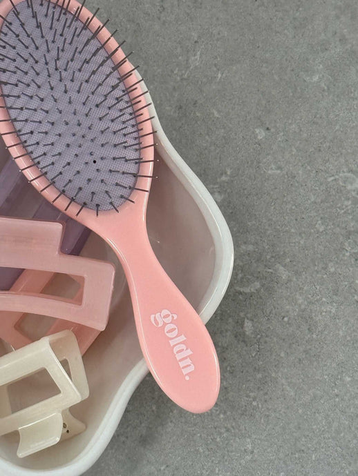 Pink hairbrush with bristle head and wooden clips on a gray surface